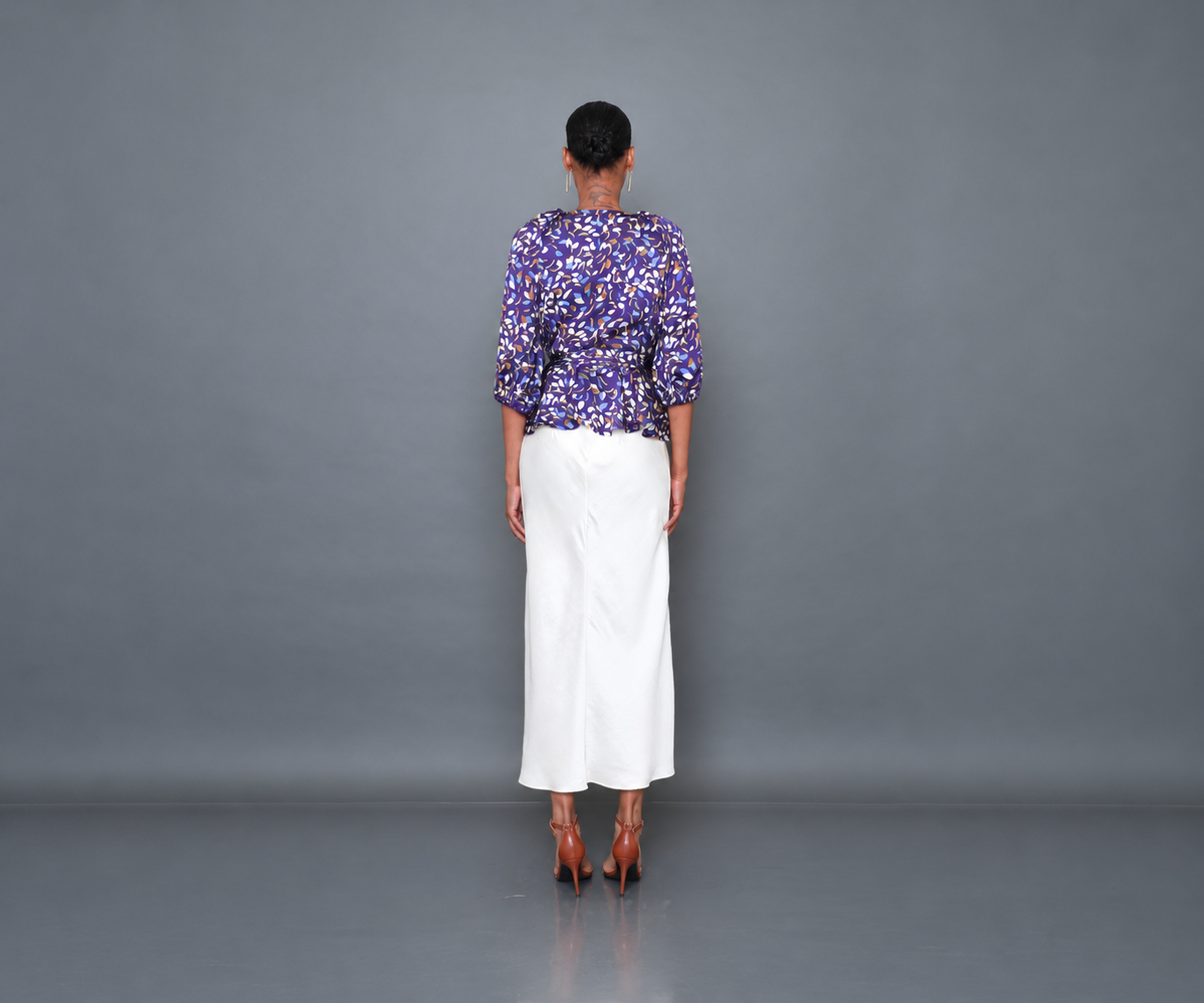 Undra Celeste New York Olivia Raglan Wrap Puff Sleeve Top in Purple Falling Leaves print, featuring luxurious hammered satin, a deep V-neckline, voluminous elbow-length puff sleeves, an adjustable wrap waist with an oversized tie sash, and a flared peplum hem. Elevated contemporary women's workwear.
