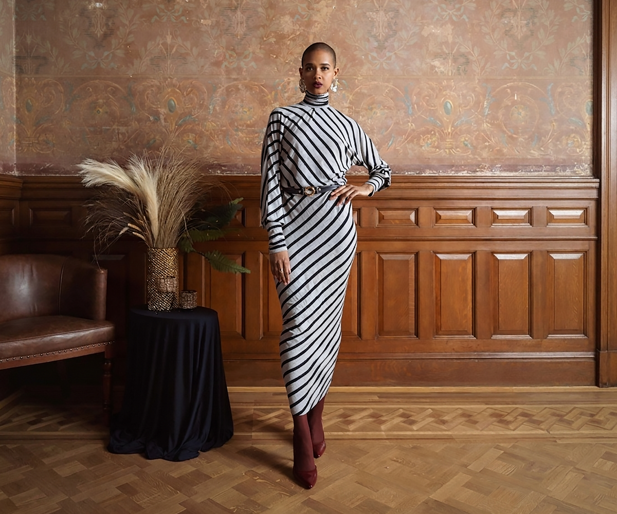 Undra Celeste New York Bias Stripe Knit Dress in Navy Grey, featuring bold diagonal stripes, a high turtleneck, voluminous long sleeves with fitted cuffs, a defined waist, and an asymmetrical midi-length hemline. Sophisticated contemporary women's workwear with modern geometric elegance.