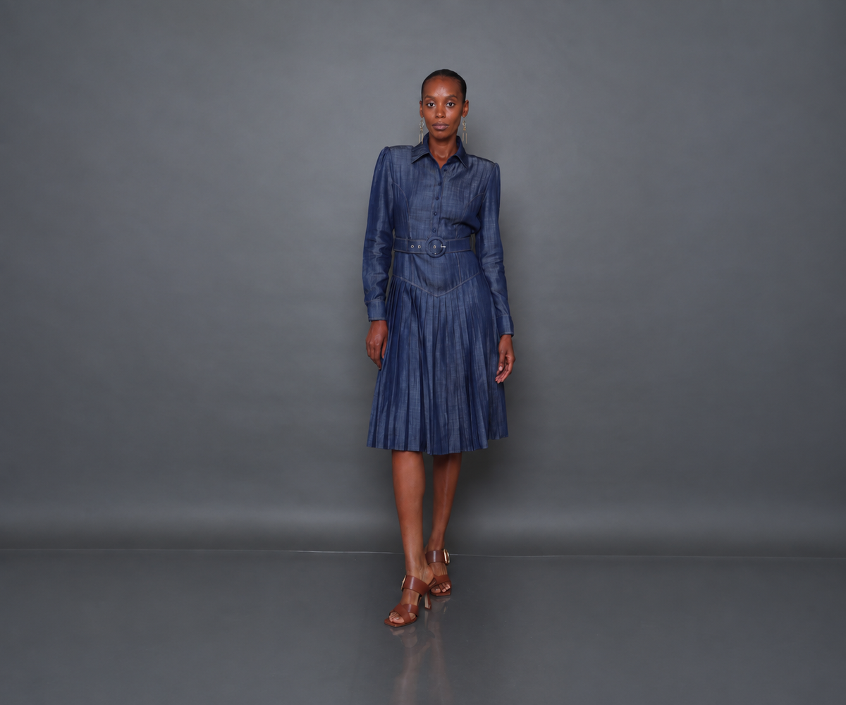 Undra Celeste New York Donna Pleated Dress in Soft Denim, crafted from soft Tencel denim, featuring a tailored button-front bodice, structured shoulders, long sleeves, a flattering V-shaped waist yoke, matching belt, and a flowing pleated midi skirt. Sophisticated contemporary women's workwear.