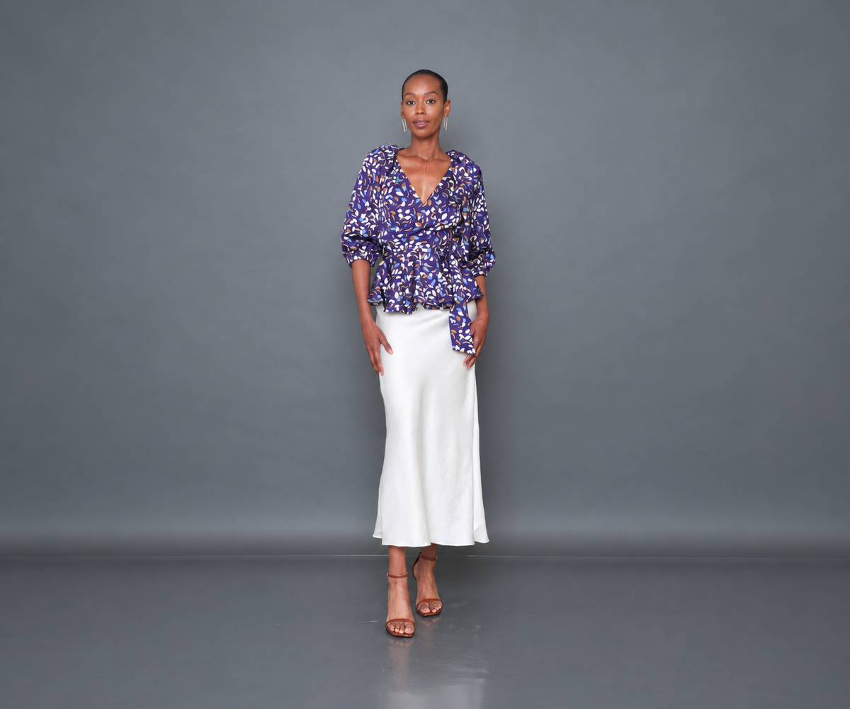 Undra Celeste New York Olivia Raglan Wrap Puff Sleeve Top in Purple Falling Leaves print, featuring luxurious hammered satin, a deep V-neckline, voluminous elbow-length puff sleeves, an adjustable wrap waist with an oversized tie sash, and a flared peplum hem. Elevated contemporary women's workwear.