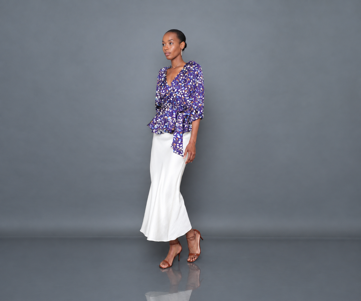 Undra Celeste New York Olivia Raglan Wrap Puff Sleeve Top in Purple Falling Leaves print, featuring luxurious hammered satin, a deep V-neckline, voluminous elbow-length puff sleeves, an adjustable wrap waist with an oversized tie sash, and a flared peplum hem. Elevated contemporary women's workwear.