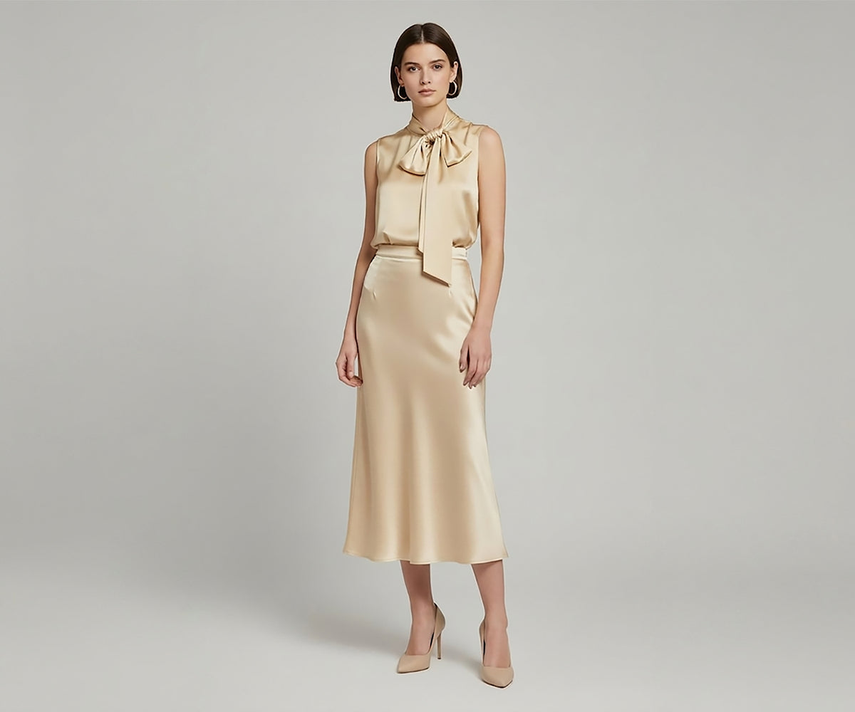 Undra Celeste New York Satin Bow Blouse in Banana Yellow, featuring a luminous satin finish, sleeveless silhouette, softly gathered neckline, oversized statement bow with cascading ties, and an elegant fluid drape. A sophisticated statement blouse for elevated contemporary women's workwear.
